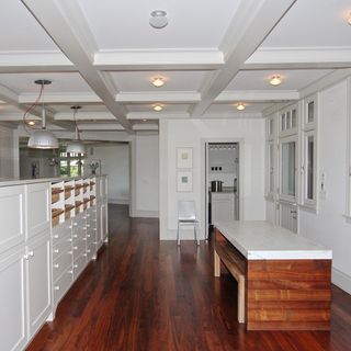 A large white kitchen prep space with conference ceiling, wooden floor, and a large free standing storage unit.