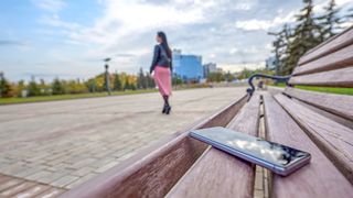 A woman walks away from a phone forgotten on a bench