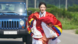 a woman wearing traditional korean clothing runs down a road in front of a jeep truck