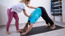 A yoga instructor makes adjustments to her pupil while they do downward dog stretch