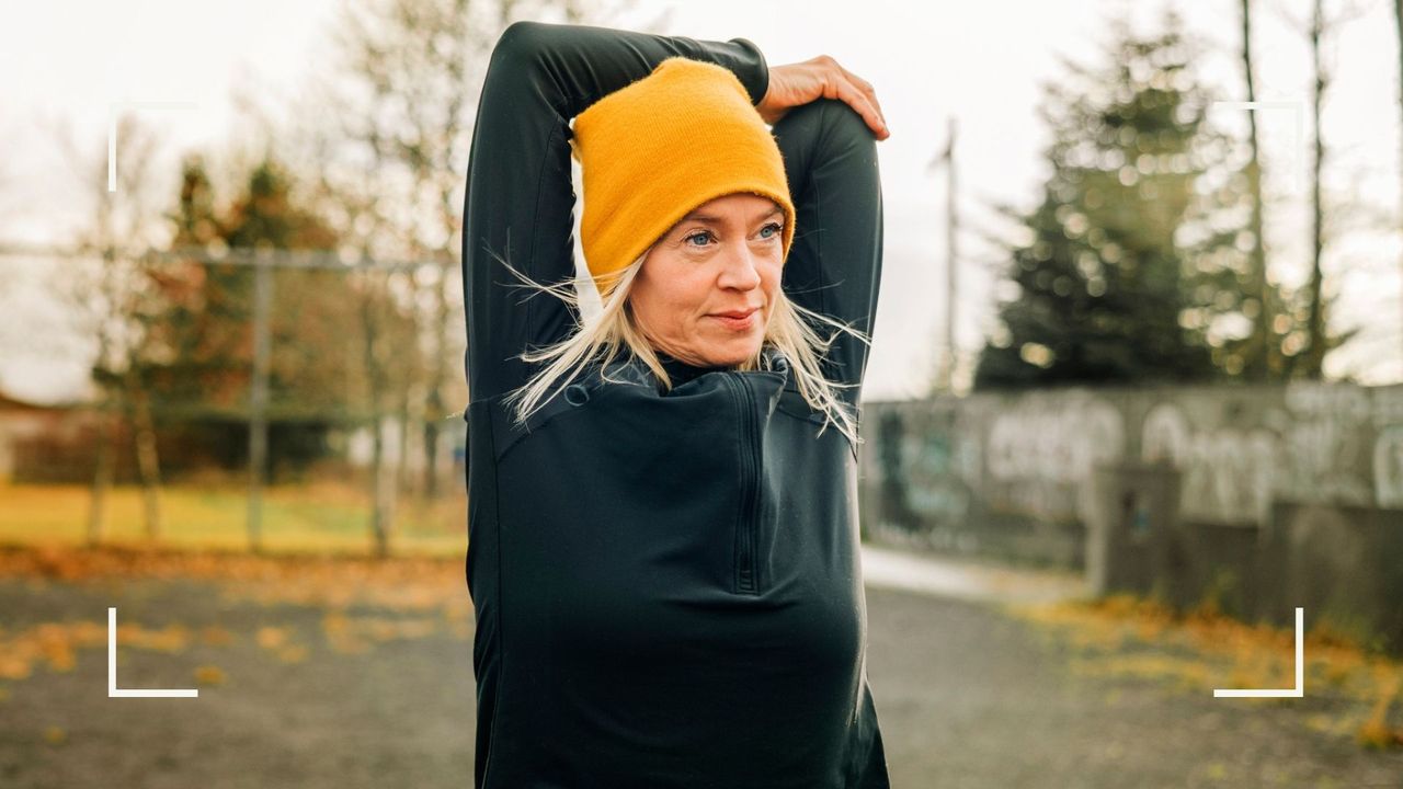 Woman wearing yellow hat stretching arms in park before working out