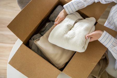 A woman putting folded clothes into a box to sell second-hand.