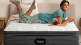 A woman wearing a green t shirt and grey jogging bottom lays on the Beautyrest PressureSmart mattress