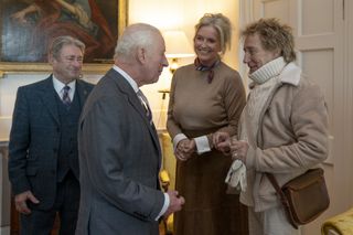 King Charles wearing a gray suit talking to Penny Lancaster and Rod Stewart, who is wearing a thick ivory turtleneck