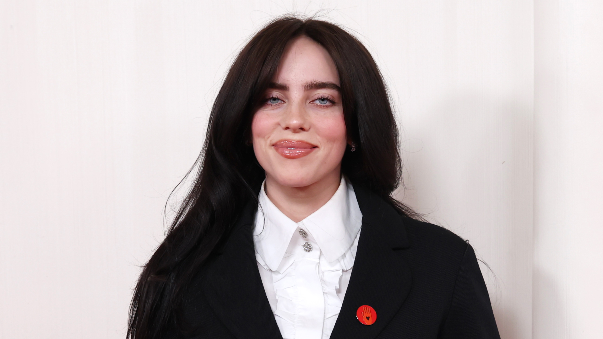 Billie Eilish wearing a white button up shirt and black blazer with red pin