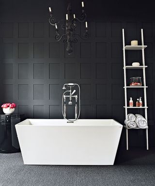 An example of bathroom lighting ideas in a black bathroom with a chandelier over a freestanding contemporary bath