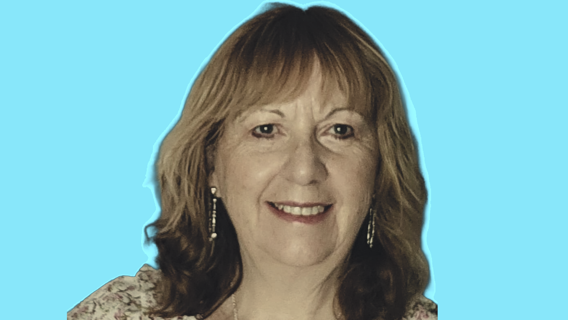 A woman with curled blonde-highlighted hair and drop earrings smiles