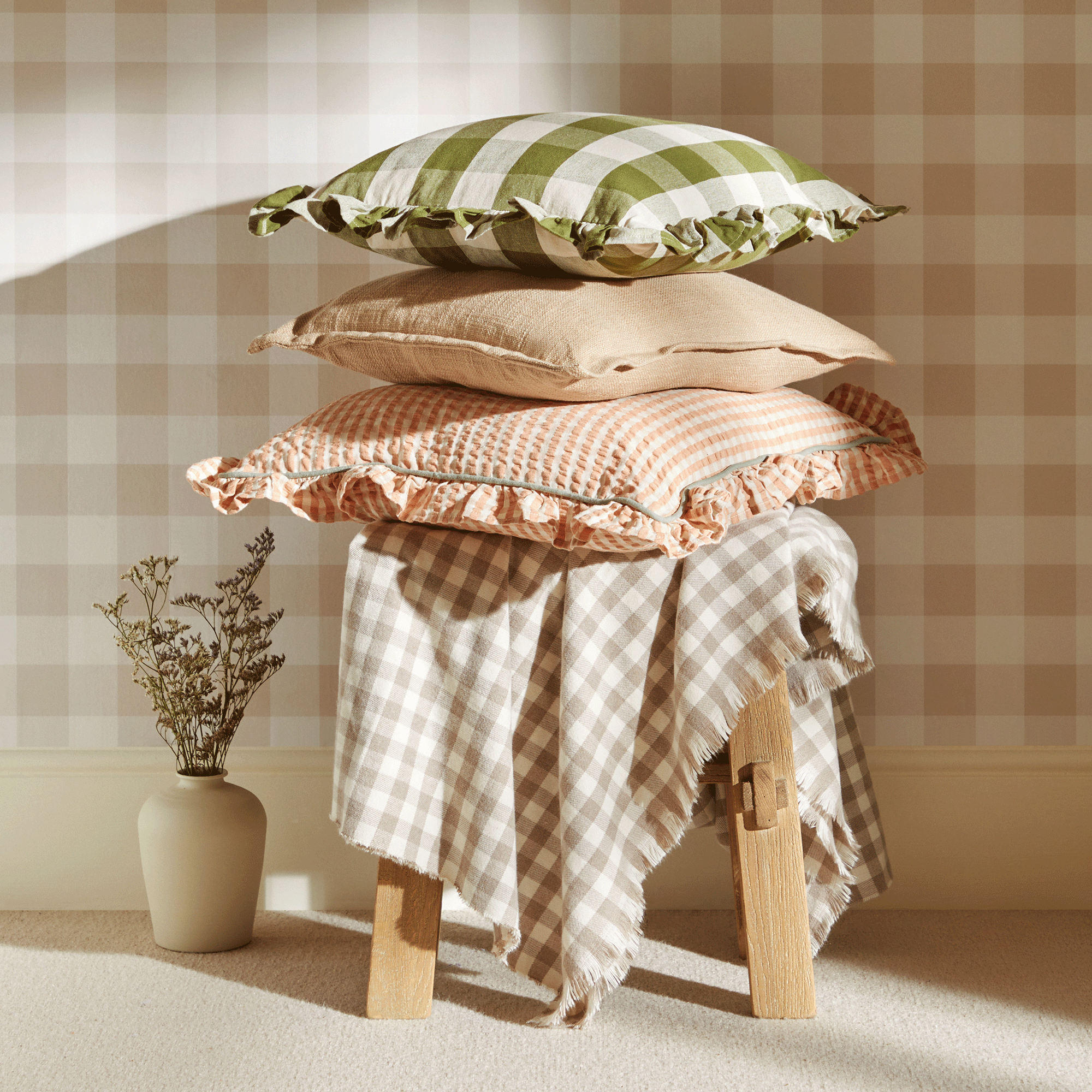 a stack of cushions and a throw in gingham prints on a wooden stool in front of a gingham wallpapered wall