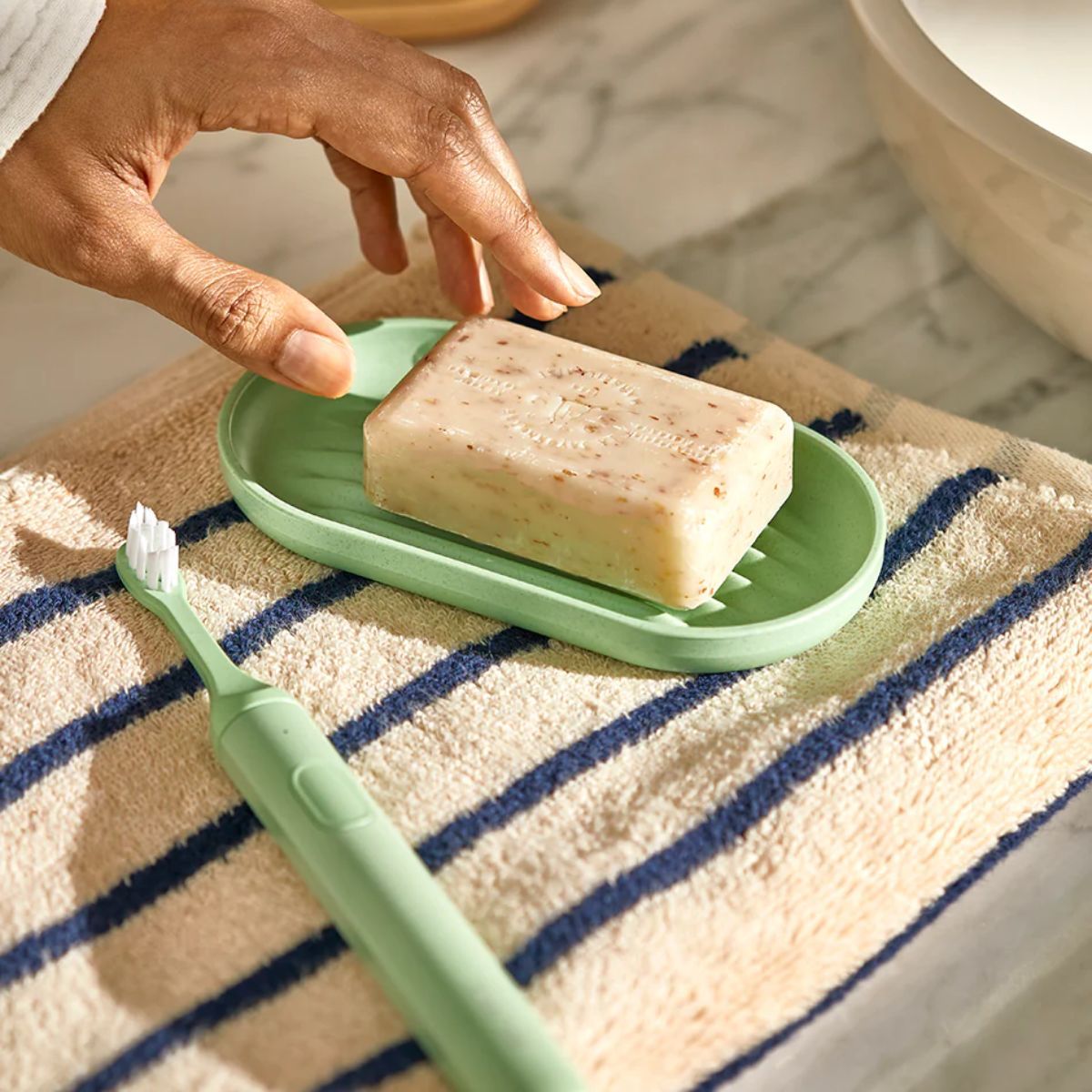 Suri green toothbrush and new soap dish on a striped towel