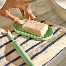Suri green toothbrush and new soap dish on a striped towel