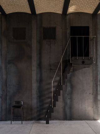 Steep, metal stairs on a dark concrete wall, lead to an opening above.