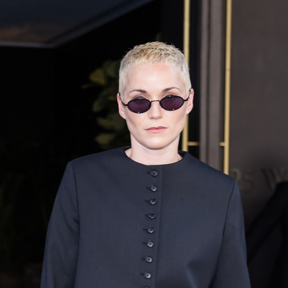 Jude Mack wearing a black blazer, blue jeans, and open-toe sandals