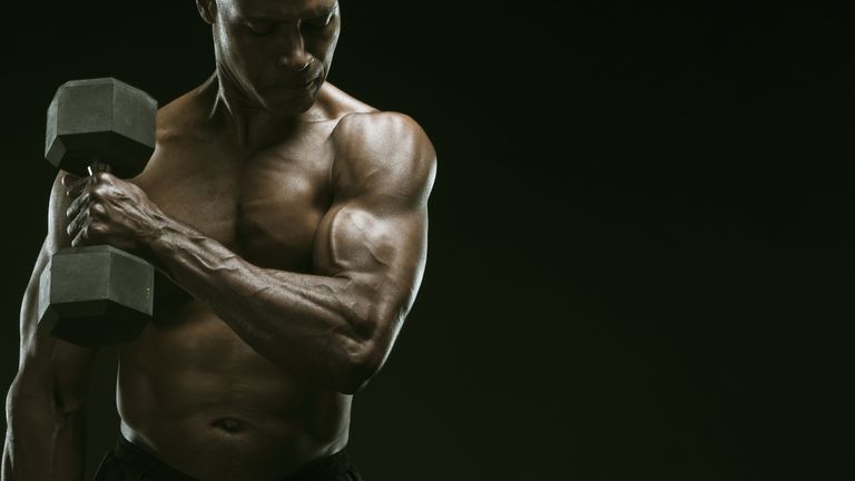 Muscular man curling a dumbbell in a photo studio in front of a dark background