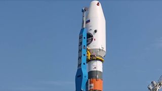 A white payload fairing sits atop a white, orange and green rocket.