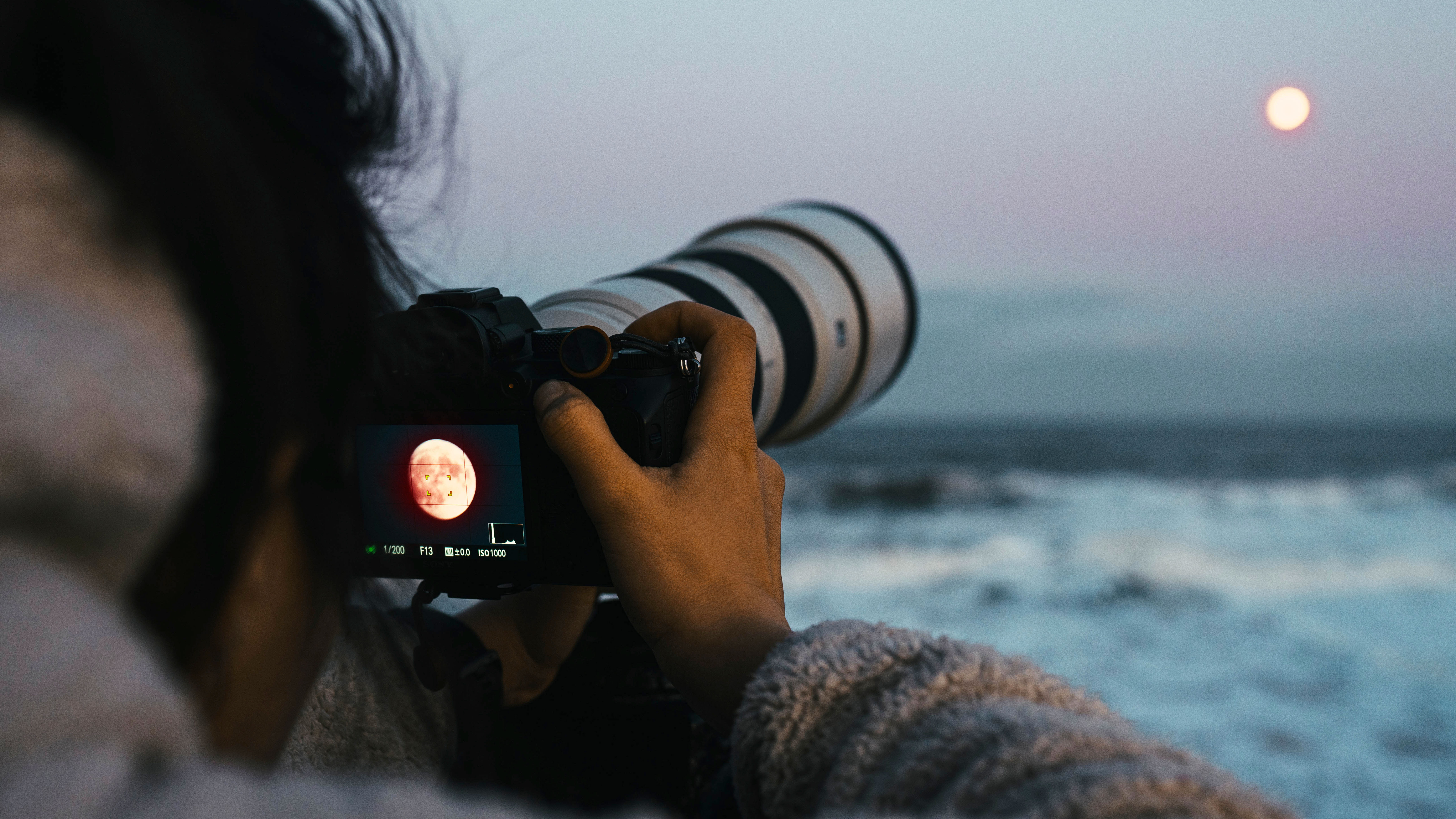 Person with a camera at the beach taking photos of the moon