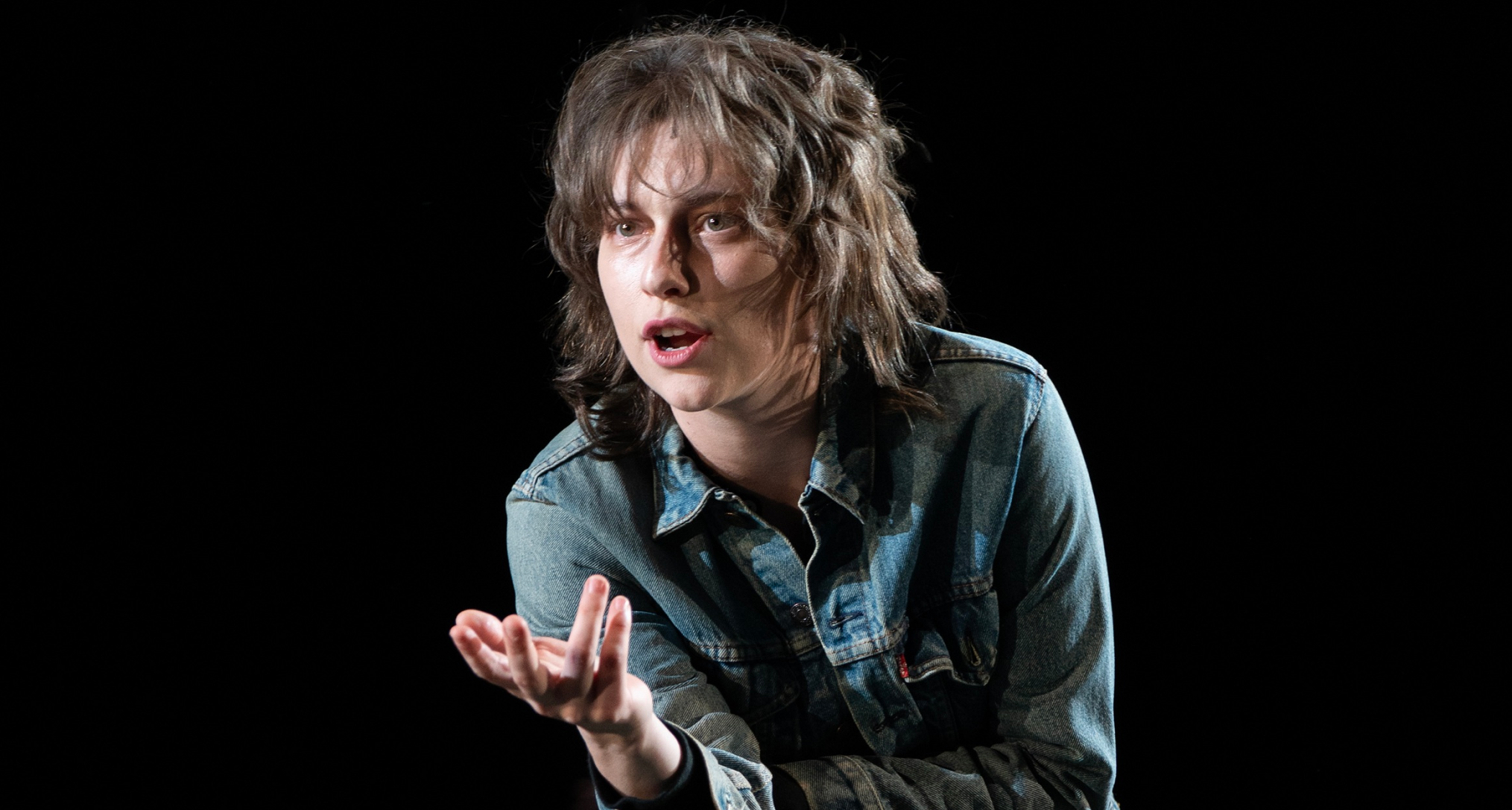 king princess as lisa wearing a shaggy wig and jean jacket on stage in the musical of girl interrupted
