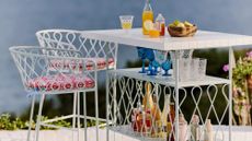 Whimsical, powdery blue South-of-France-style outdoor bar furniture styled beachside with patterned seat cushions and assorted bar accessories.