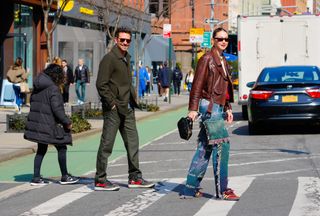 Bradley Cooper and Gigi Hadid smiling and crossing a NYC street wearing coats and jeans.