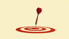 A dart that has landed in the middle of a bullseye on a red target