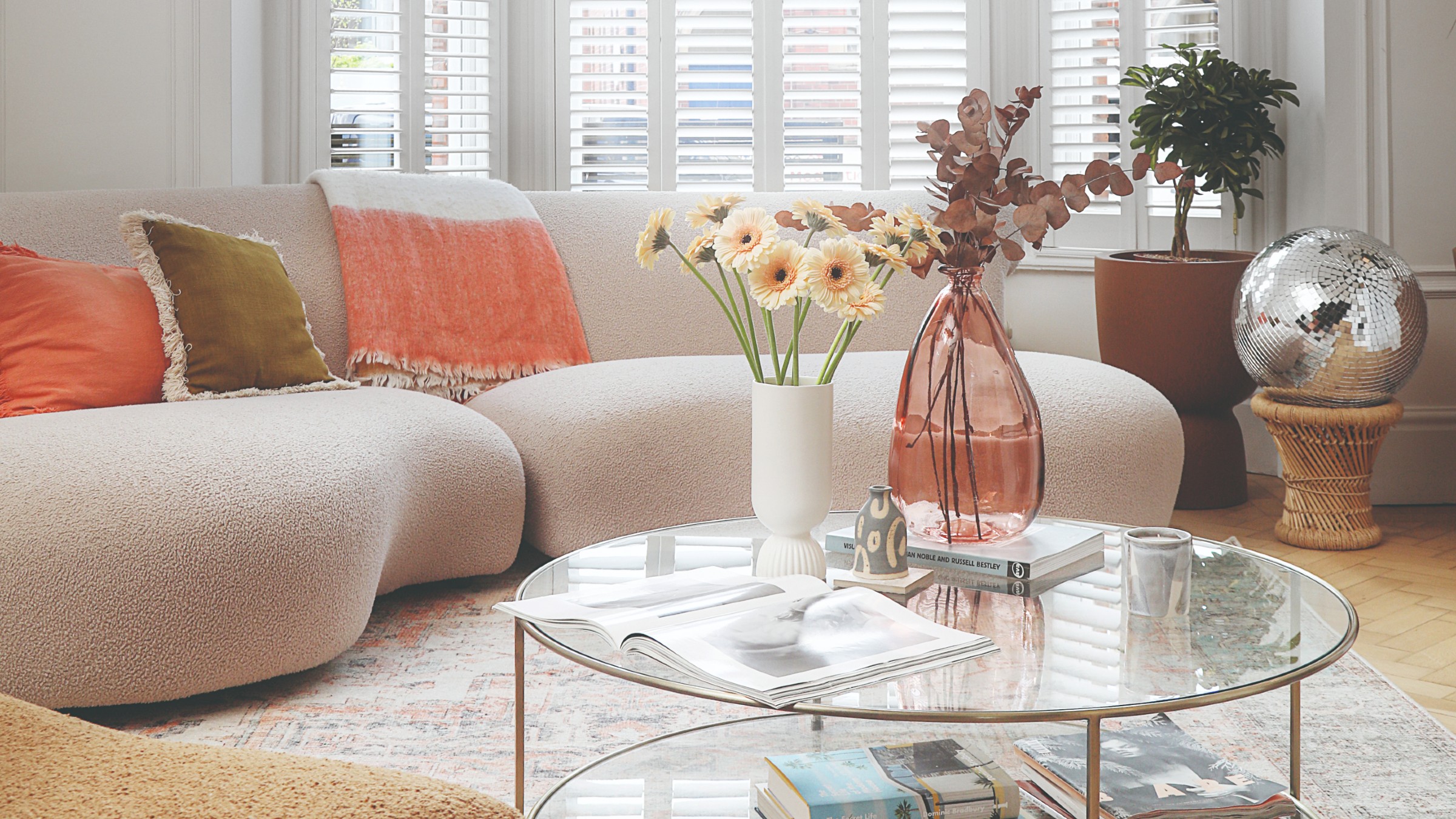 A white living room with a curved sectional sofas in off-white upholstery and a round glass coffee table in front of it