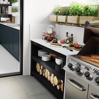 outdoor kitchen with white work top, BBQ, log storage, tableware storage, wooden boxes with herbs