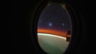 a view through a porthole in a spaceship showing the two Magellanic clouds in outer space