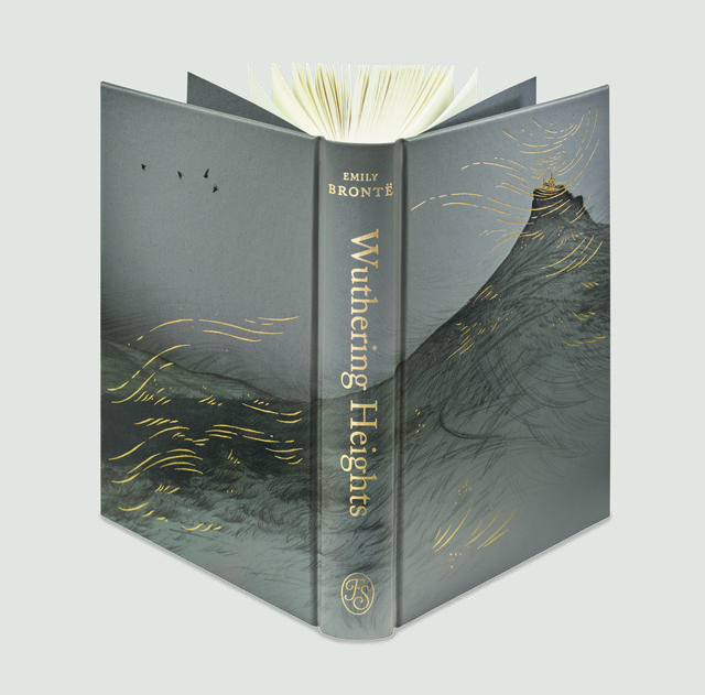 A high-end hardcover edition of Wuthering Heights is shown partially open, featuring a grey cloth binding with gold-foiled illustrations of a windswept, dark moor and a distant manor on a hill.
