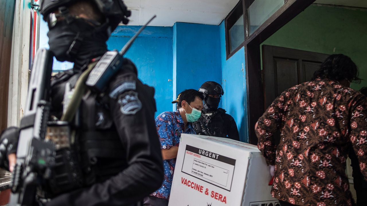 Workers unload Sinovac vaccines from a truck under police escort.