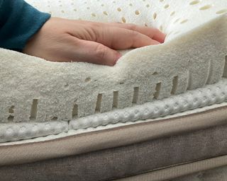 Paige Cerulli, a white woman, demonstrating lack of edge support on the Turmerry latex mattress topper by placing her hand on the edge of the product