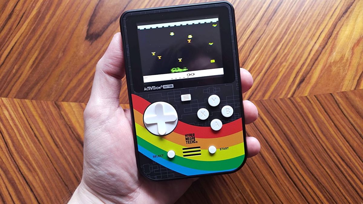 Hand holding Super Pocket Activision Edition over woodgrain table with Dragonfire gameplay on screen.