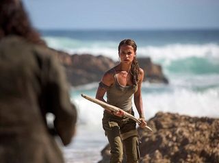 Alicia Vikander as Lara Croft wielding piece of driftwood on beach