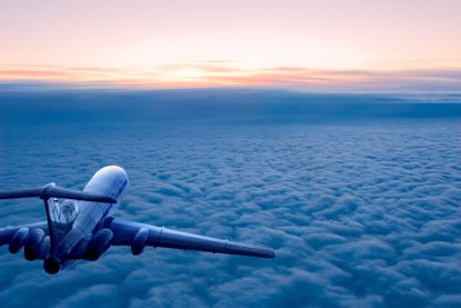 An airplane at sunrise flying over the clouds, away from the camera