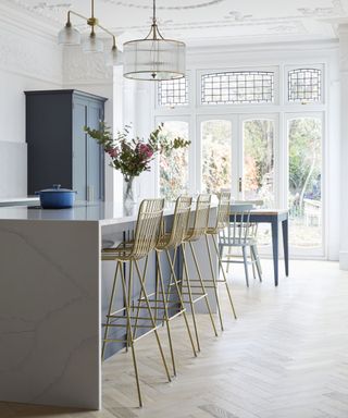 long grey kitchen island with long breakfast bar style side and gold framed stools