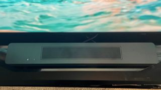 Bästa soundbar: Den nya Bose Soundbar 600 står på en TV-bänk framför en TV som visar blått vatten på skärmen.