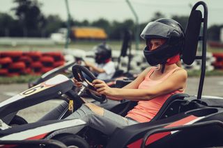 A go karting track shows a woman in a helmet ready to start the race.