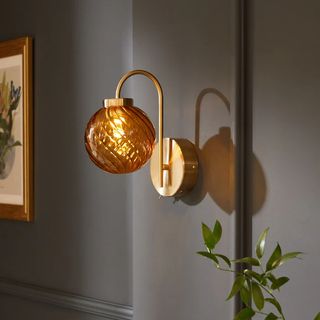 wall light with brass base and curved arm, organge glass patterned shade