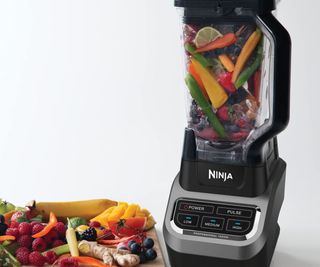 A Ninja blender filled with fruit beside a plate of berries.