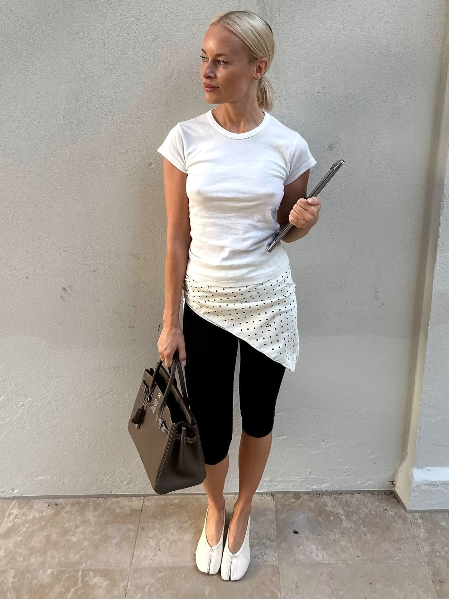 Danish style influencer and designer Thora Valdimars poses in a white T-shirt polka-dot print hip belt scarf, black capri pants, a brown Hermes bag, and white Martine Margiela Tabi shoes