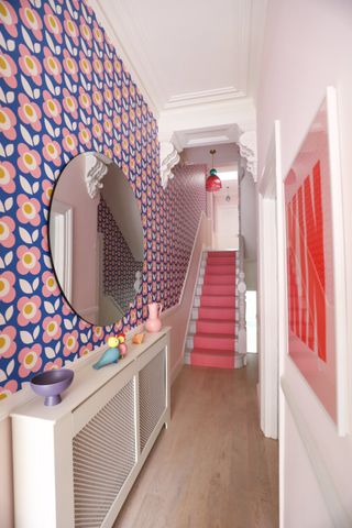 Daisy chain wallpaper in pink and blue in bright hallway with circular wall mirror