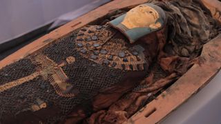 We see a mummy with a decorated face mask within a coffin.