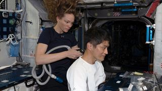 a woman in a blue shirt uses an electric shaver to trim the hair a japanese man with a white shirt while in microgravity aboard a space station
