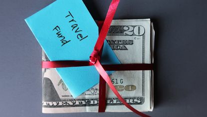 A stack of cash bills tied with a ribbon and labeled "travel fund."