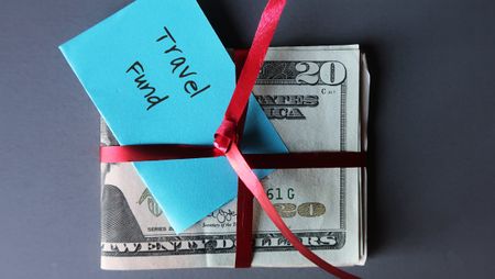 A stack of cash bills tied with a ribbon and labeled "travel fund."
