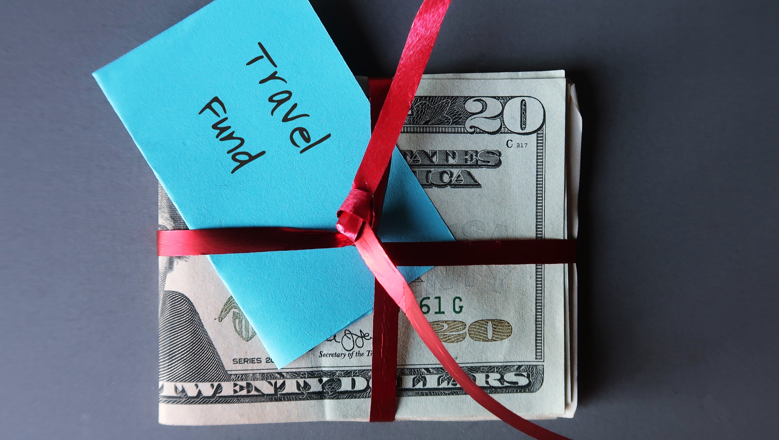 A stack of cash bills tied with a ribbon and labeled "travel fund."
