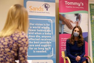 Kate Middleton wearing a blue dress and face mask talking to a blond woman at a child bereavement charity