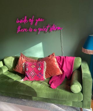 Green wall and green velvet sofa with hot pink scatter pillows, and matching, personalized pink neon quote light on wall.