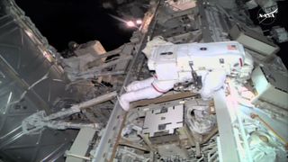 an astronaut in a white spacesuit works along a truss outside a space station