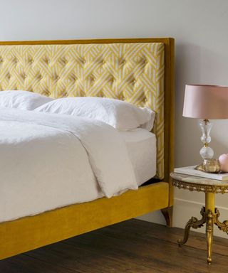 A yellow bed with white bedding and a gold nightstand with a pink lamp