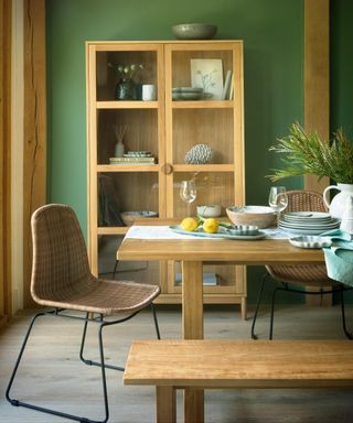 Sage green painted wall, glass-front wood cabinet, and coordinating table and bench.