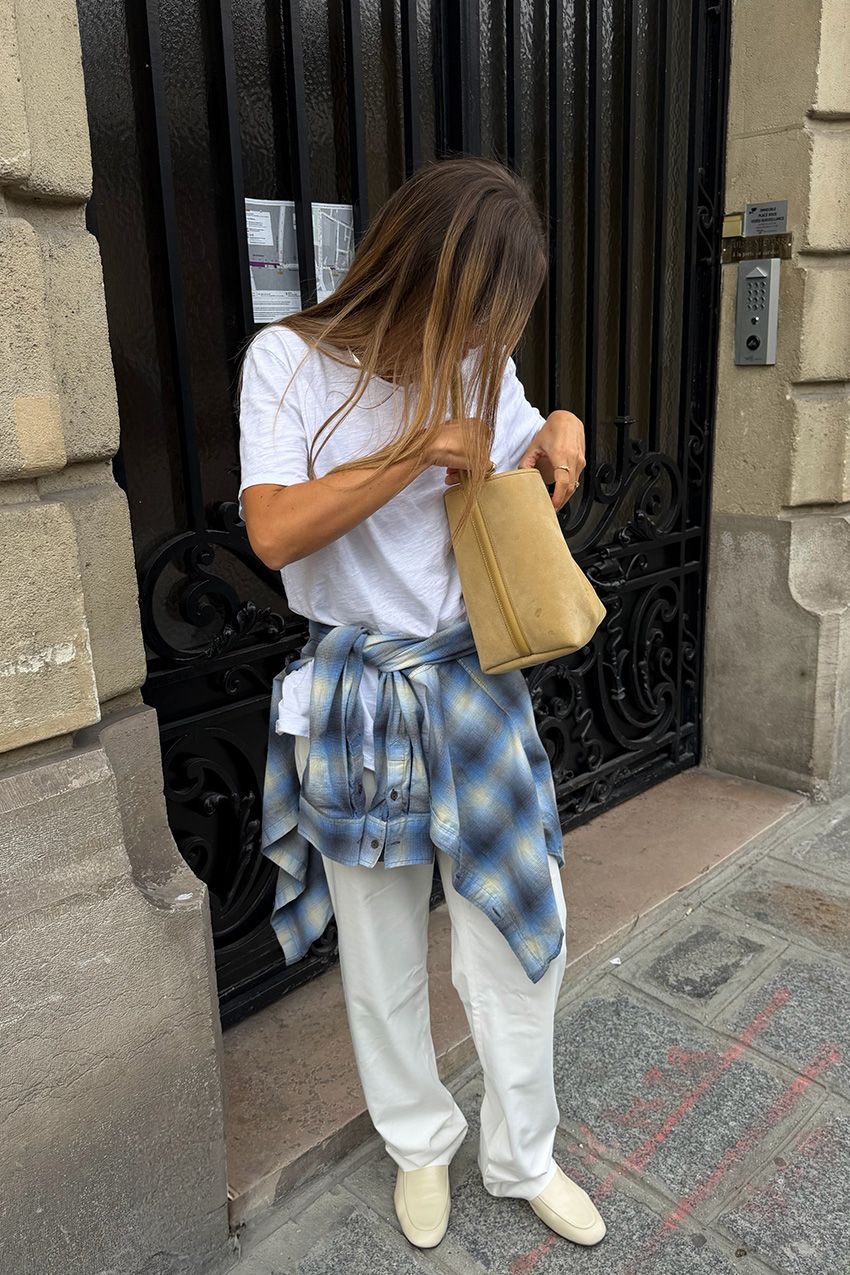 One of the biggest fall shoe trends in Paris is shown in a photo of a woman wearing a pair of soft loafers with a white t-shirt, blue flannel, baggy jeans and a suede tote